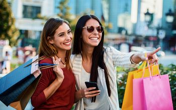 Two ladies out shopping together. Both are holding bright colored shopping bags and smiling.at Fountains of Fair Oaks, California, 95628